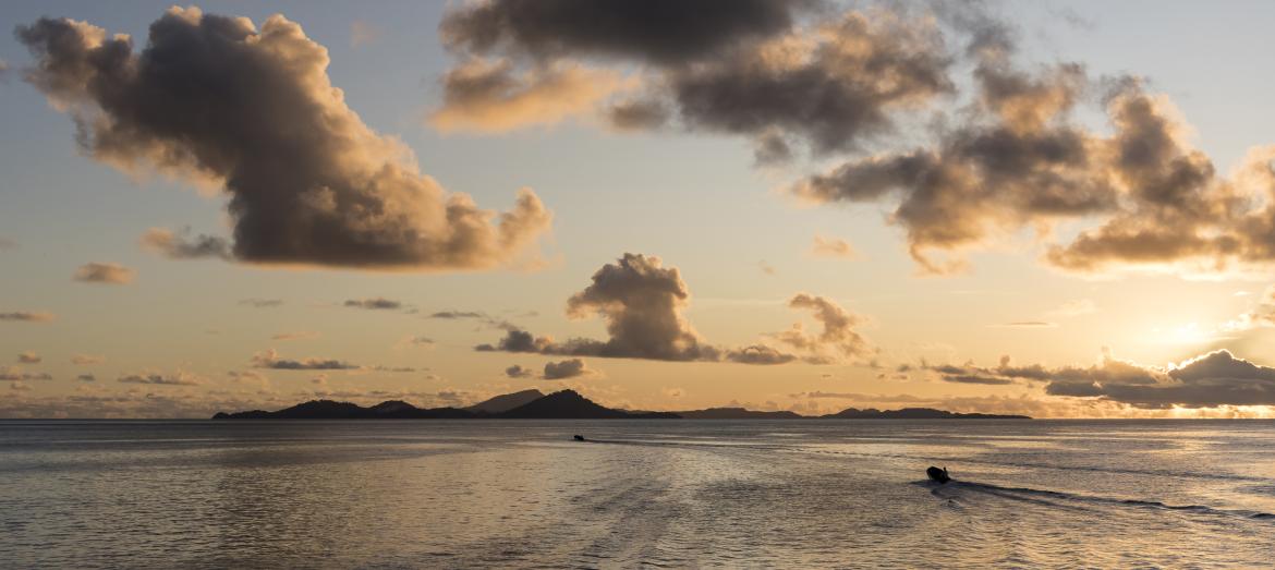 A water taxi interrupts the reflections of colorful sunset cloud formations over Truk Lagoon.